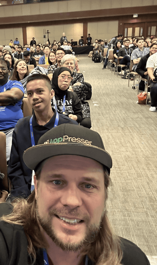 Brian Messenlehner in a green AppPresser hat taking a selfie in front of a large seated conference crowd