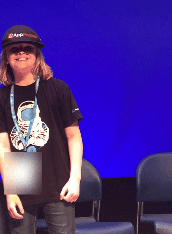 A smiling young child in an AppPresser hat and an astronaut T-shirt standing on a stage