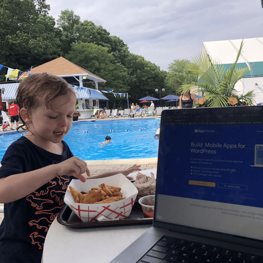 A young child eating chicken fingers by a pool next to a laptop showing the AppPresser website
