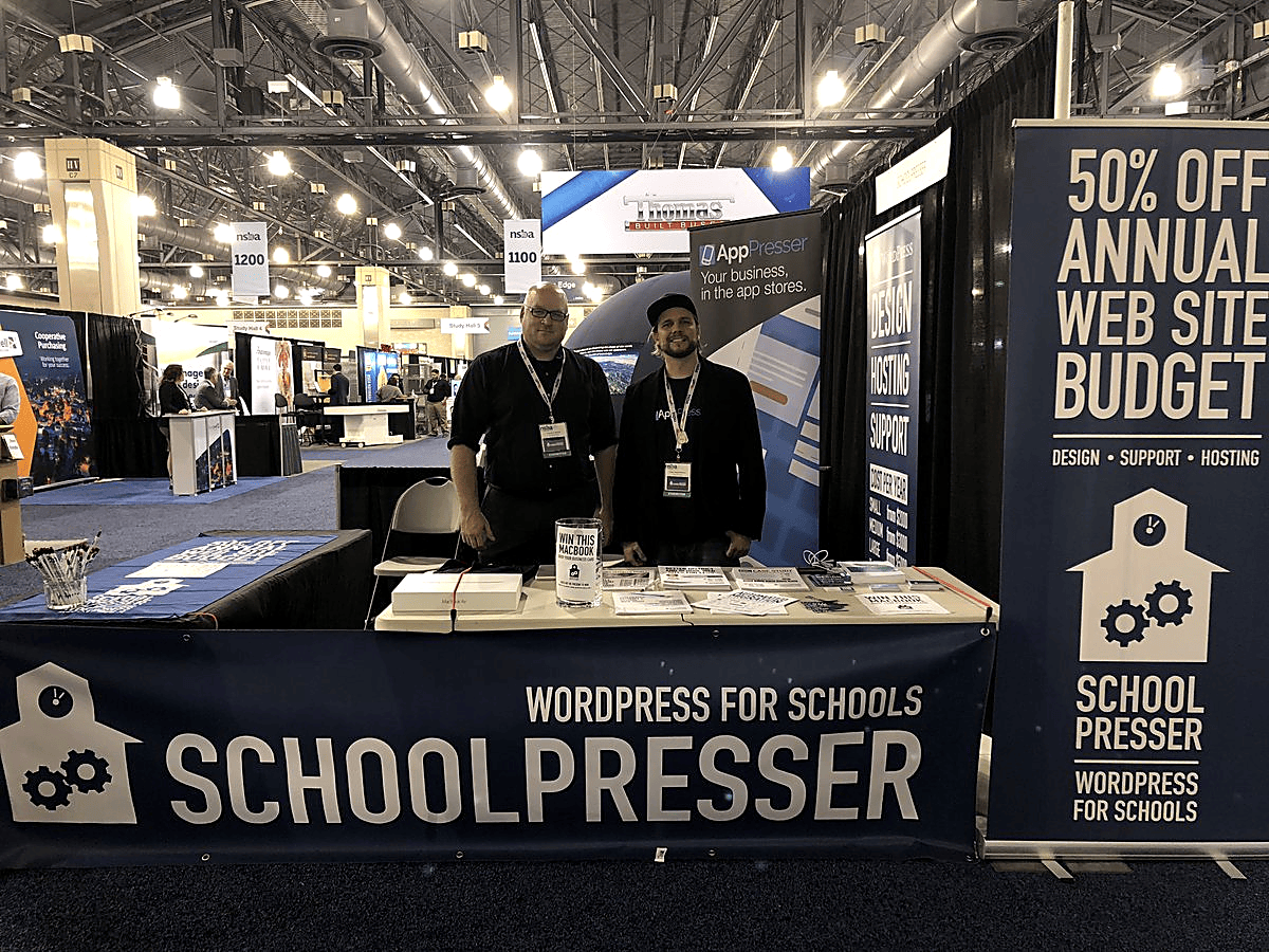 Brian Messenlehner at the SchoolPresser WordPress for Schools booth with banners for WordPress design hosting and support