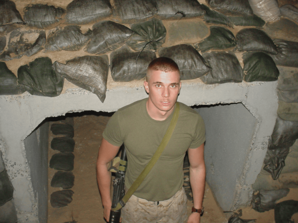 Brian Messenlehner with his rifle slung, standing in front of a sandbagged concrete bunker entrance