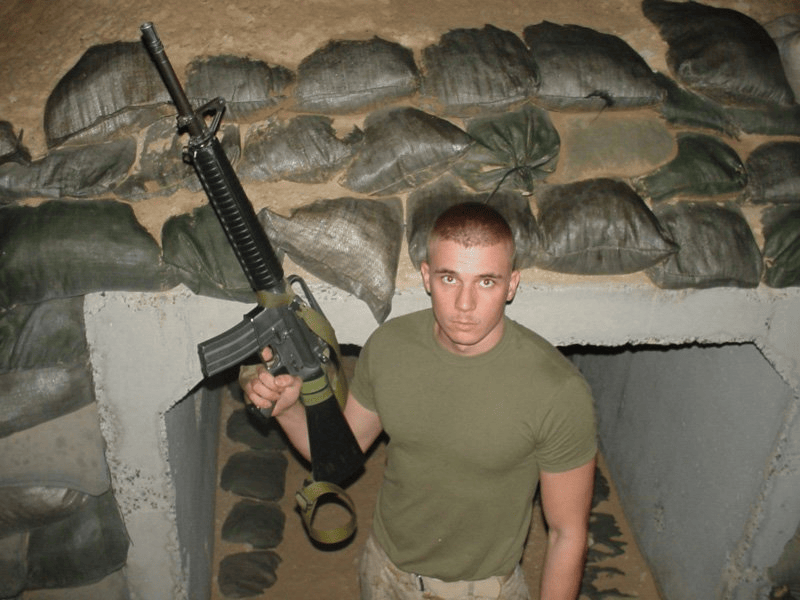 Brian Messenlehner holding his rifle at the entrance of a sandbagged concrete bunker