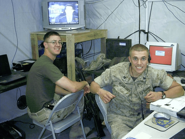 Brian Messenlehner, right, in desert camouflage at a computer workstation inside a tent during Operation Iraqi Freedom, with another Marine seated beside him
