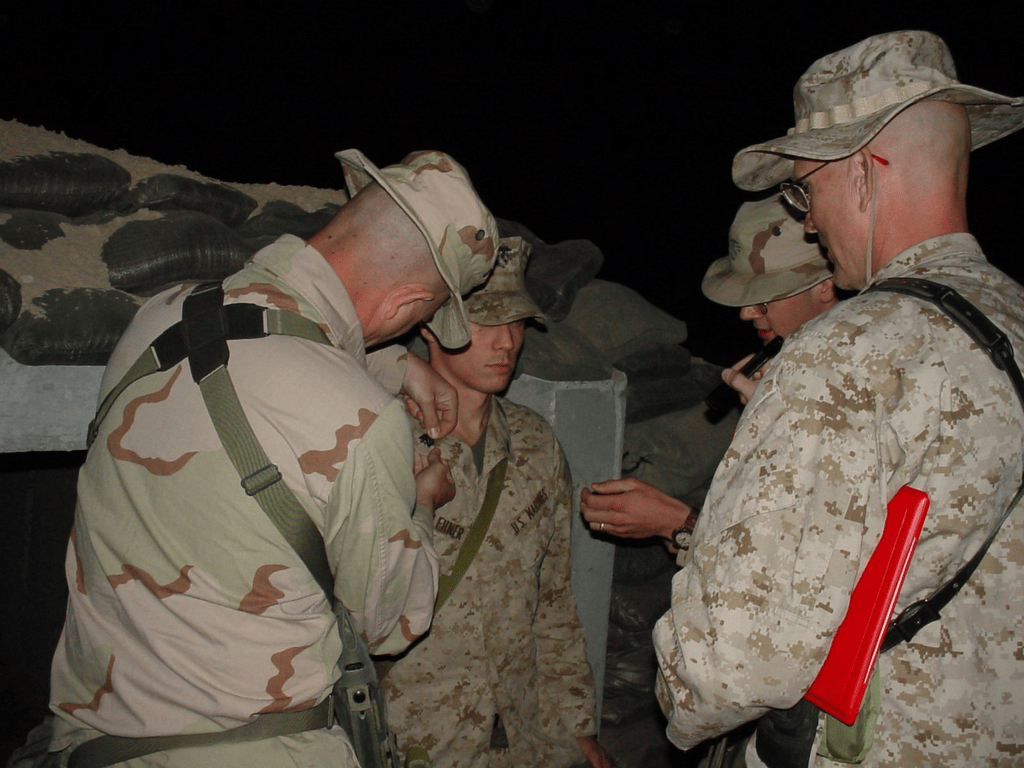 Brian Messenlehner having his sergeant chevrons pinned on at night beside a sandbagged bunker, with other Marines around him
