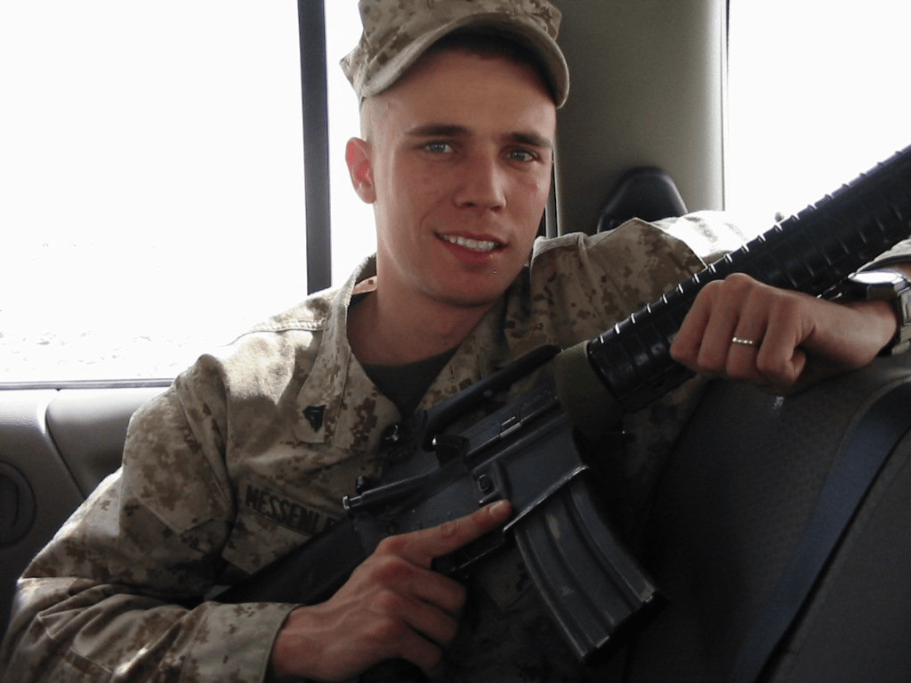Brian Messenlehner as a Marine Corps sergeant in desert camouflage, smiling in a vehicle with his rifle