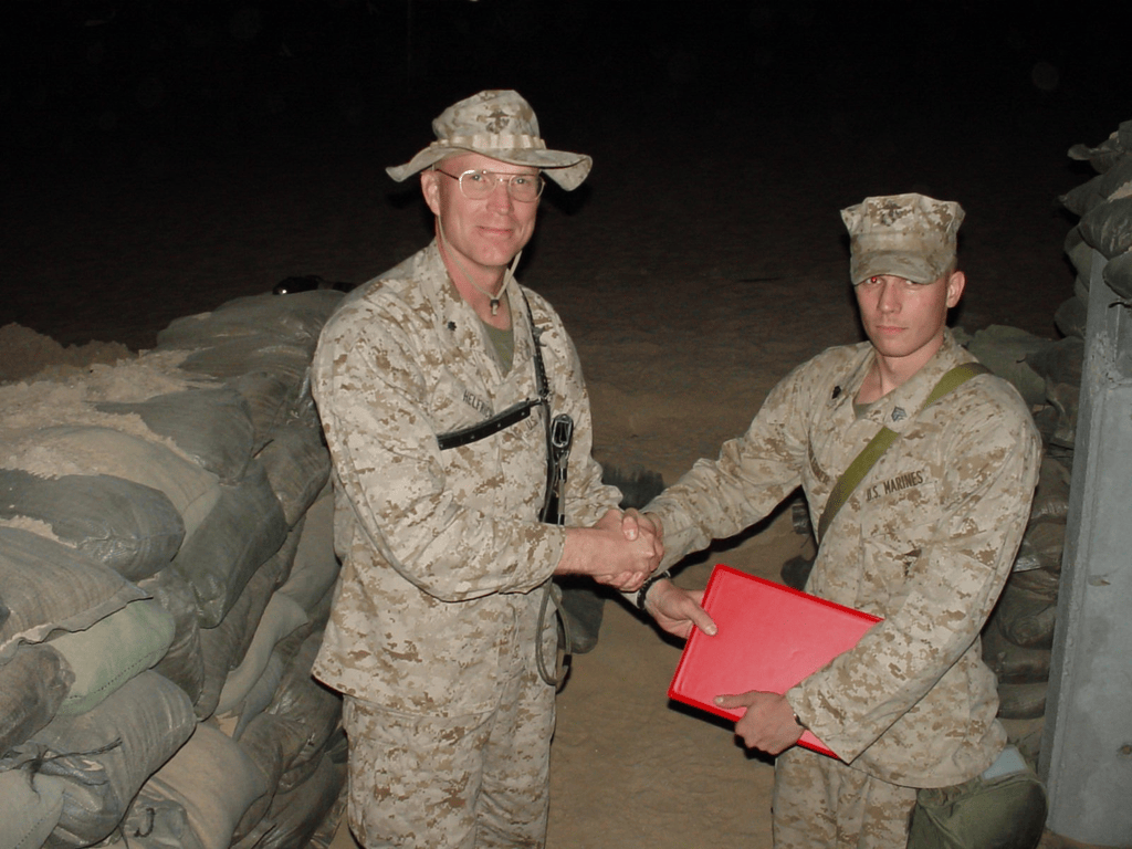 Brian Messenlehner shaking hands with an officer at night beside sandbags while holding a red folder