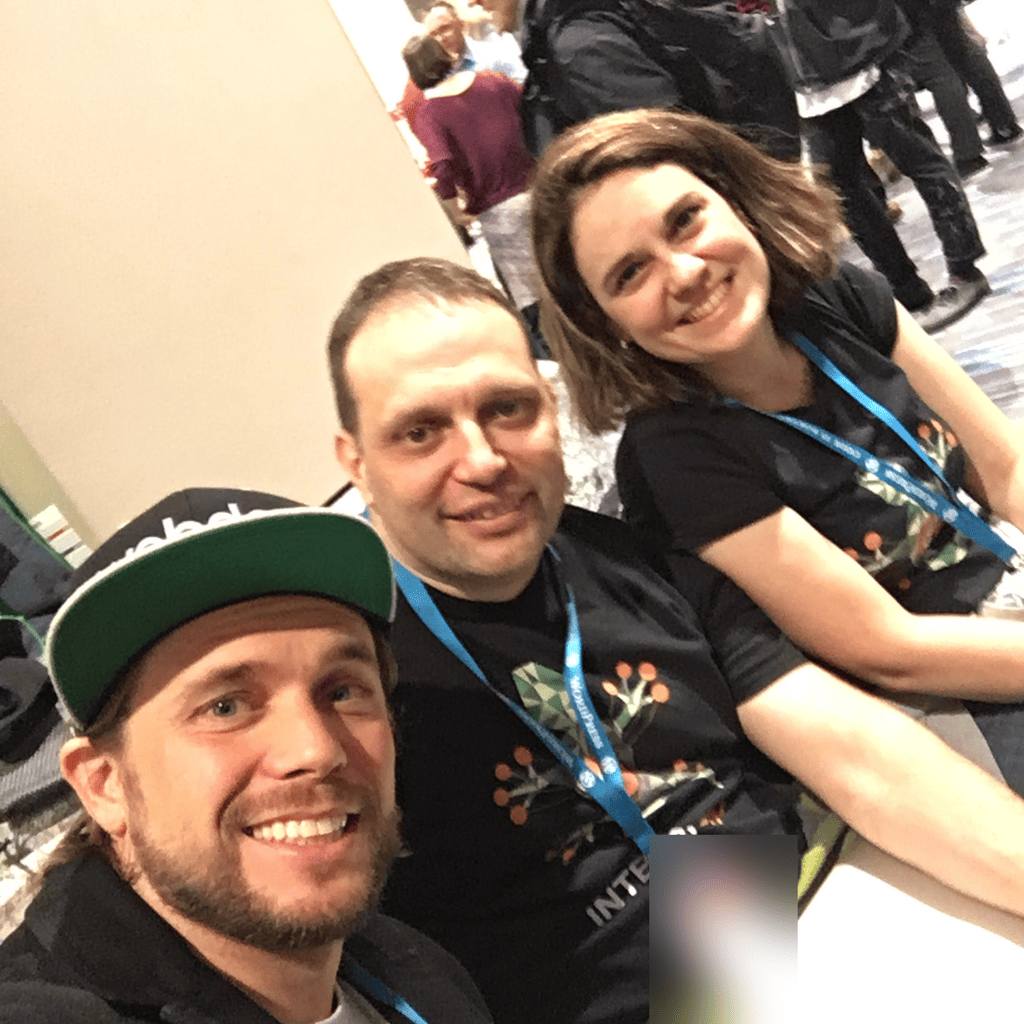 Brian Messenlehner in a WebDevStudios hat taking a selfie with two attendees wearing WordPress lanyards