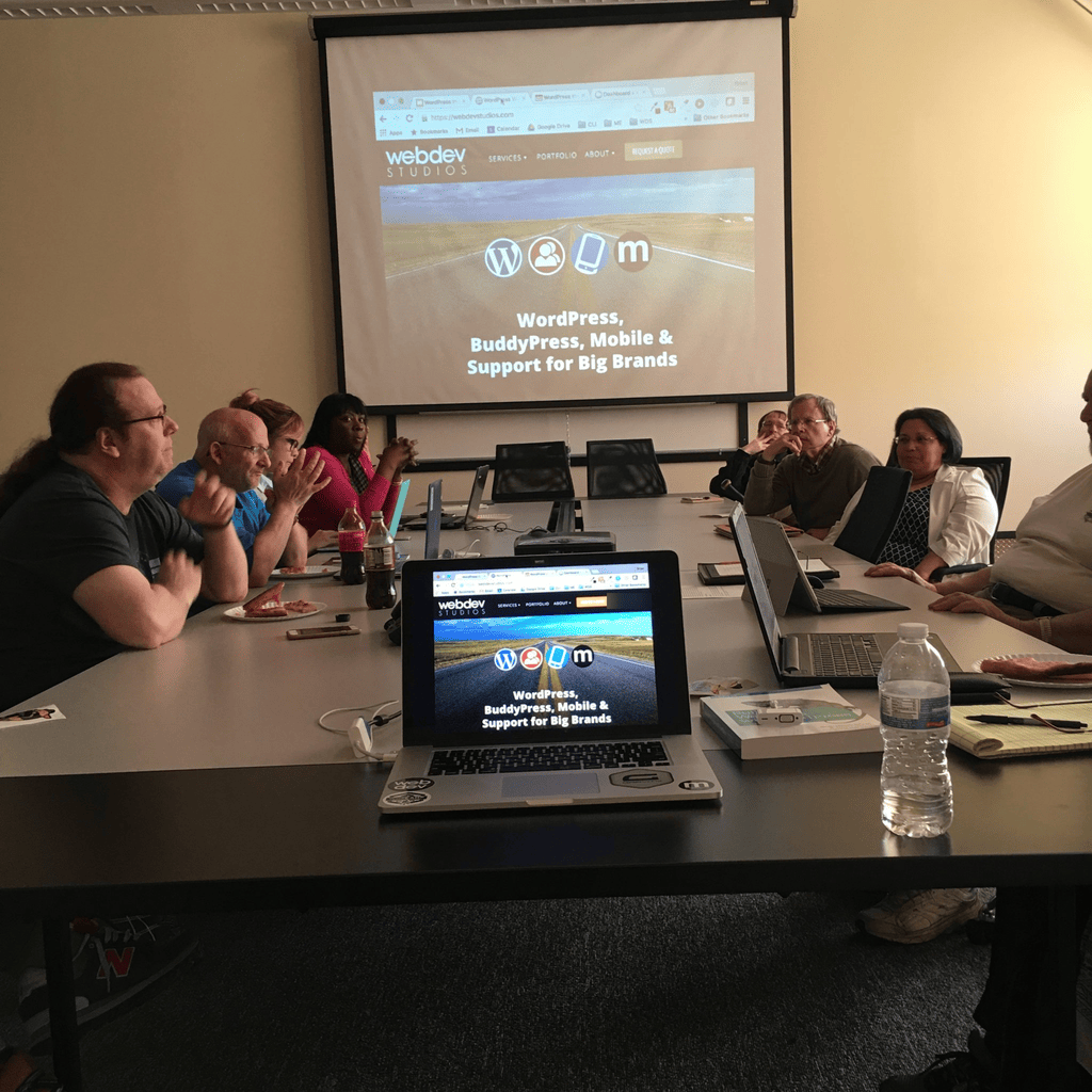 A meeting around a conference table with the WebDevStudios WordPress agency website on the projector screen and on a laptop