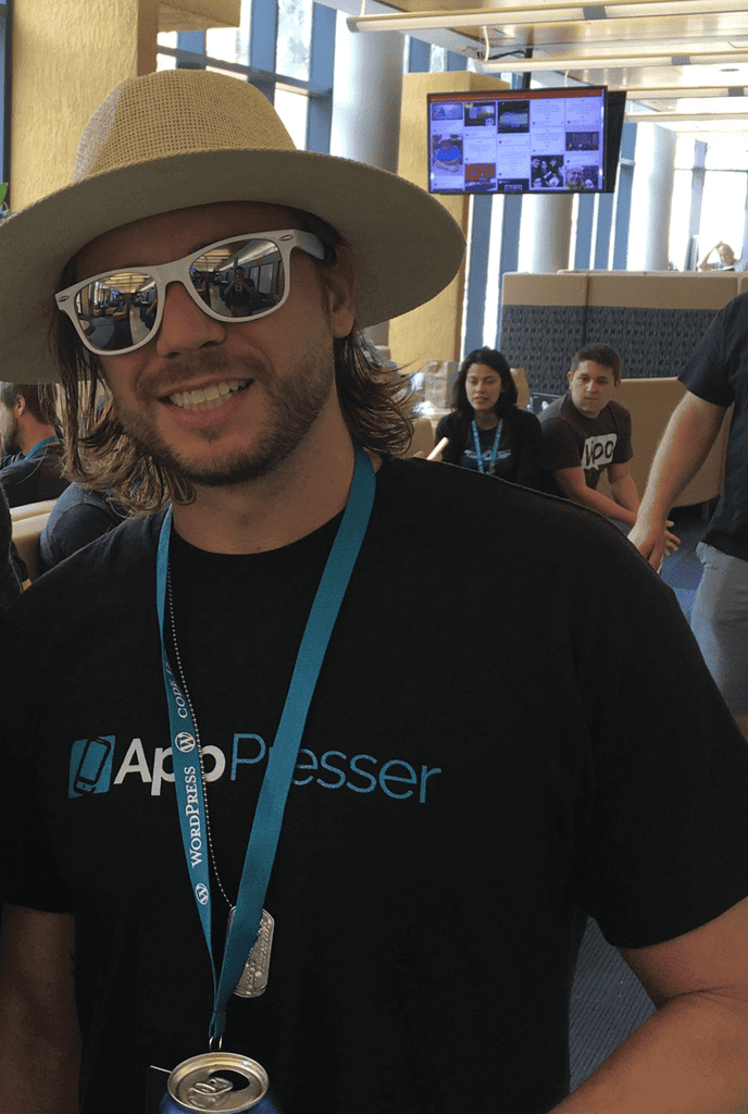 Brian Messenlehner in a straw hat, white sunglasses, an AppPresser shirt and a WordPress lanyard