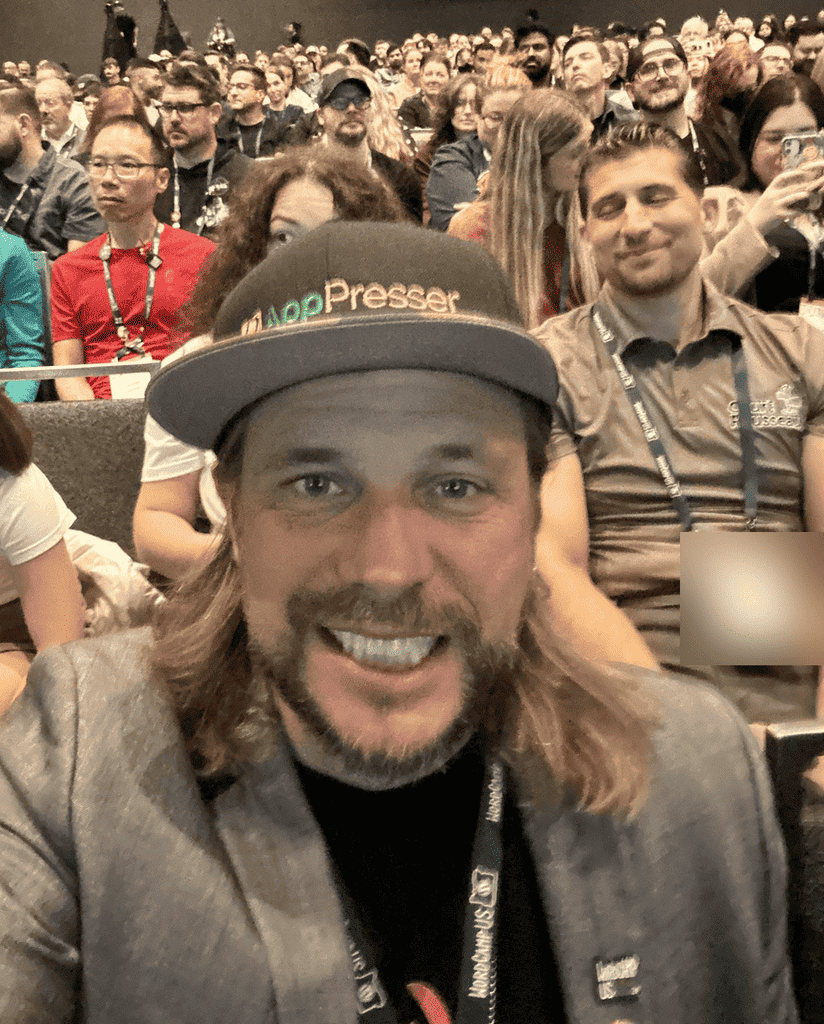 Brian Messenlehner in an AppPresser hat and a WordCamp US lanyard taking a selfie with the seated crowd behind him