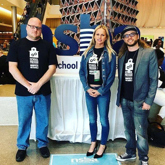 Three members of the SchoolPresser team in WordPress for Schools shirts in front of the NSBA sign at the San Antonio conference