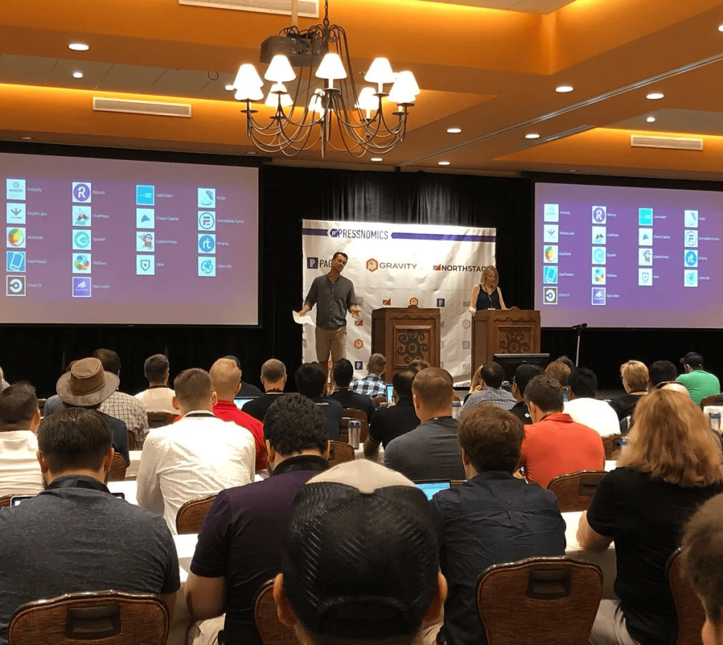 A presenter on stage at PressNomics 6 in front of a seated audience